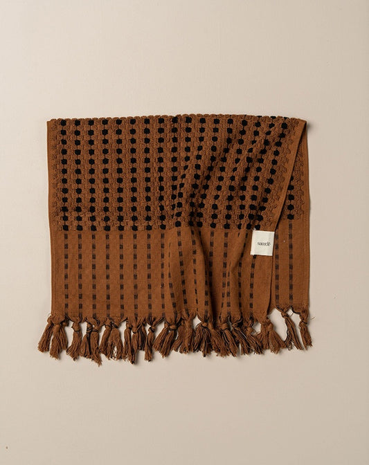 Brown woven blanket with black patterns and fringes on a beige background