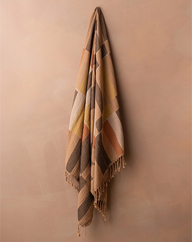 Plaid blanket with fringes hanging against a beige wall