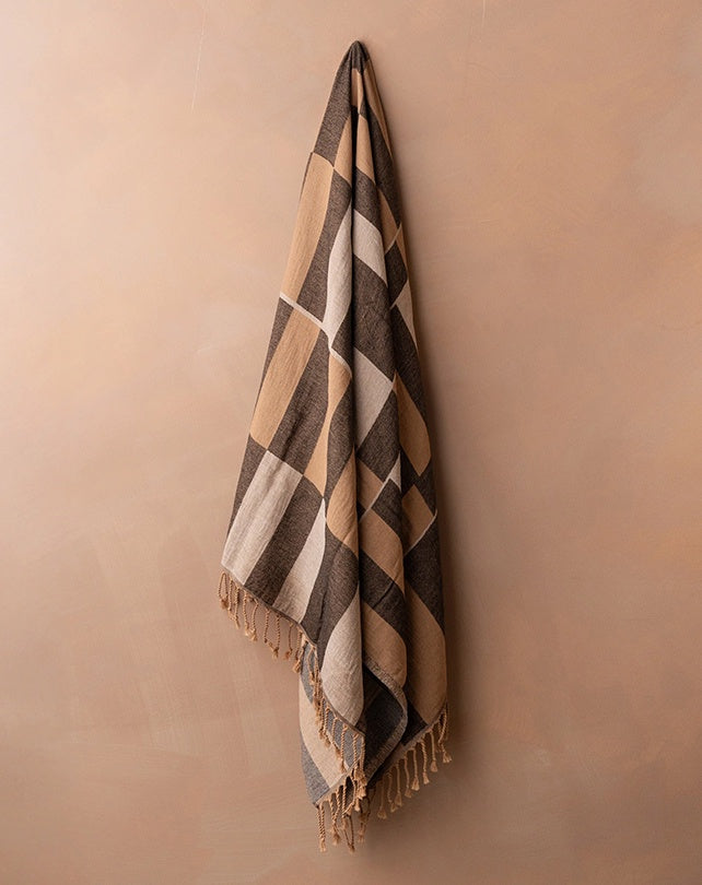 Checkered towel with fringes hanging on a beige wall