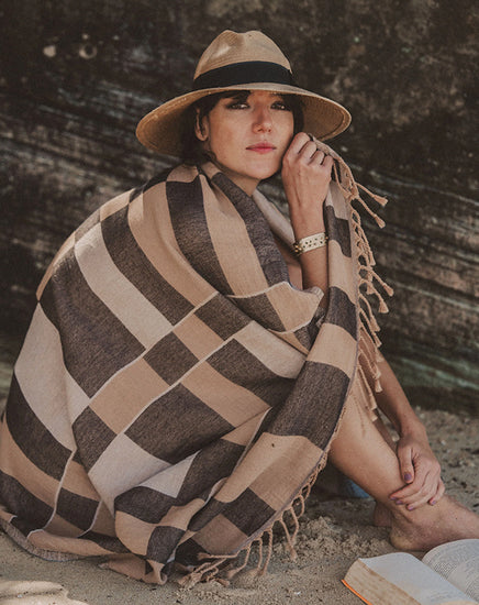 Woman sitting on a beach with a patterned blanket and hat