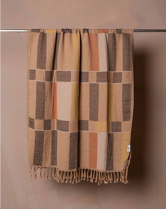 Plaid blanket with brown and beige colors hanging on a rod against a beige wall.