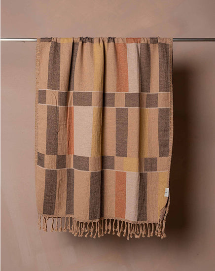 Plaid blanket with brown and beige colors hanging on a rod against a beige wall.