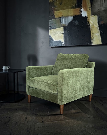 Green armchair in a room with a dark wall and abstract painting