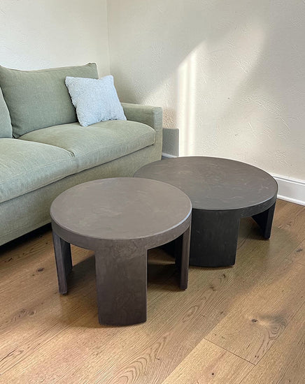 Two gray concrete coffee tables in front of a light gray sofa with a white wall background.