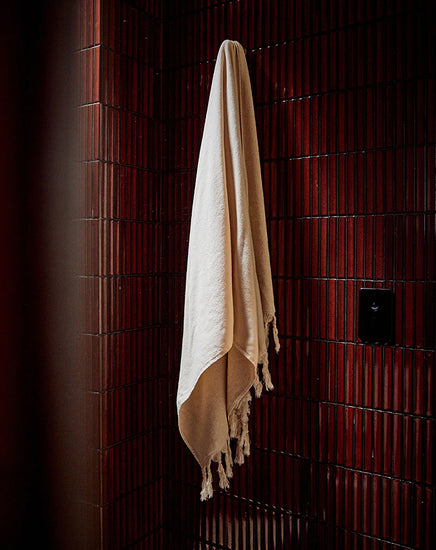 Beige towel hanging on a wooden rack against a dark wooden wall.